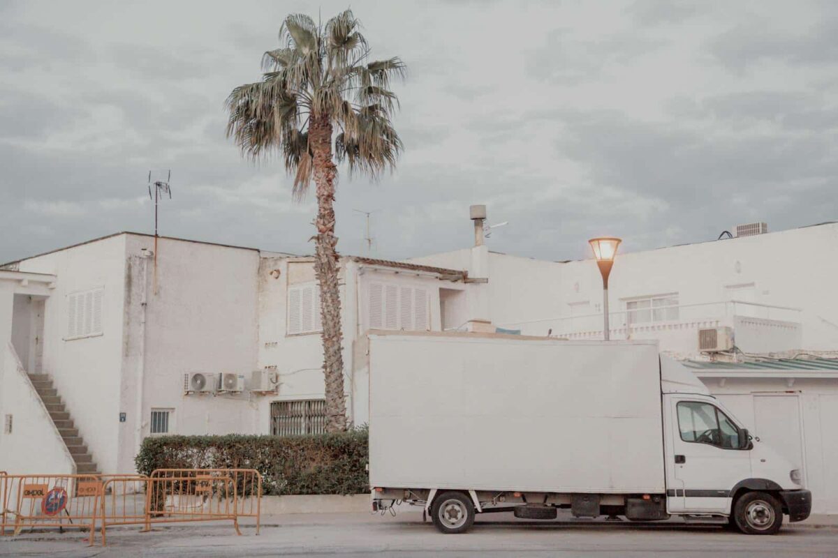 White delivery truck parked next to a white building with a palm tree in an urban setting.