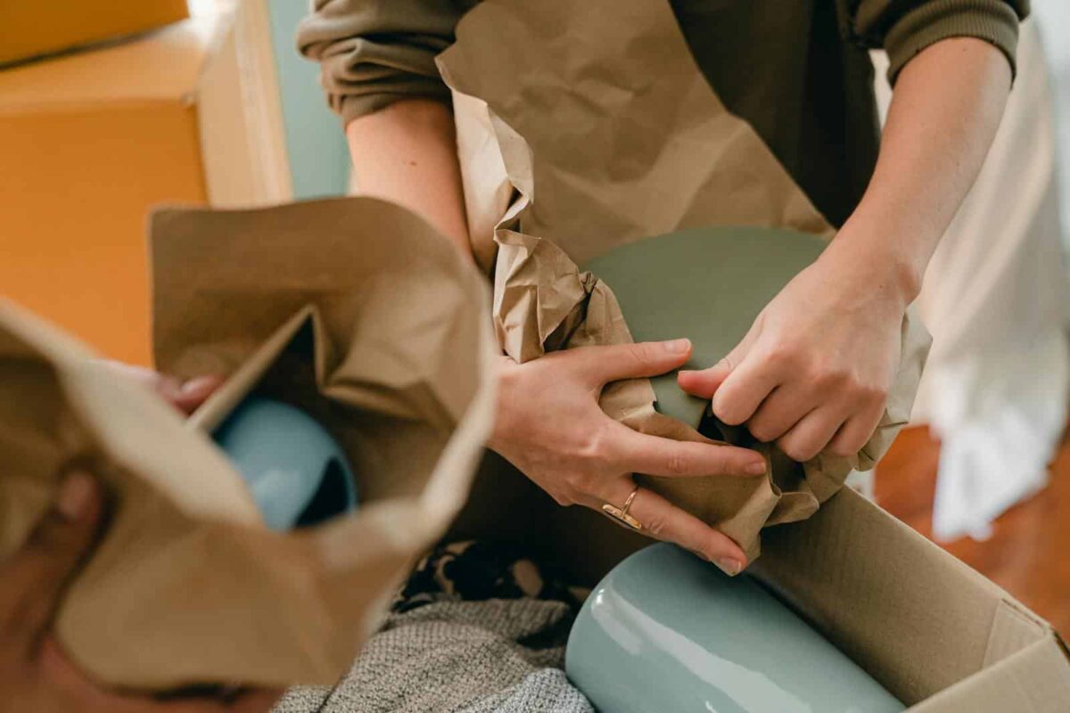 Closeup of hands carefully unwrapping ceramic items during a moving process indoors.