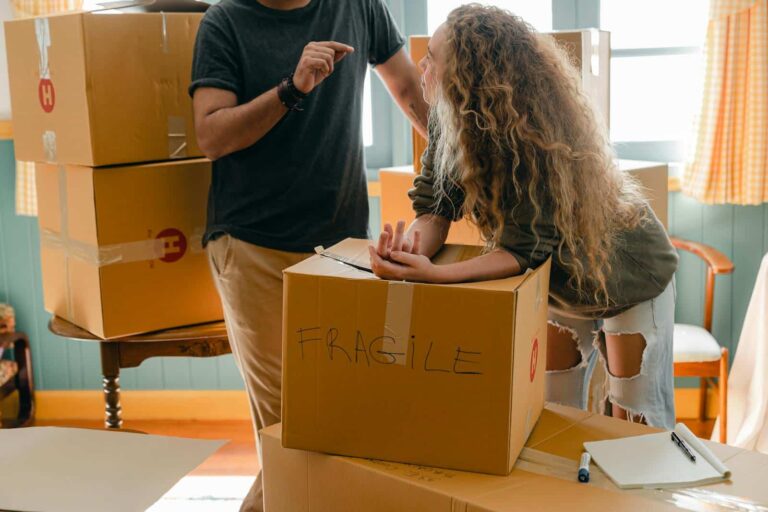 A couple engaged in packing cardboard boxes labeled 'fragile' in their new home.