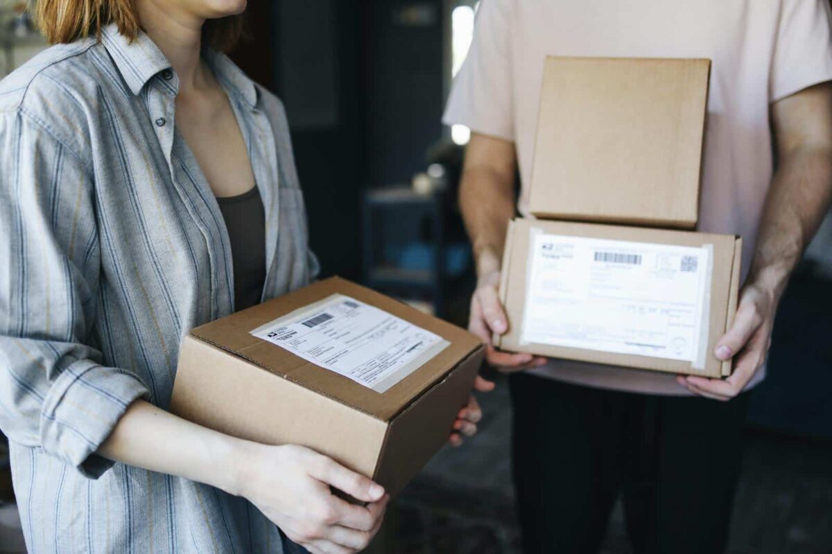Two people exchanging cardboard packages indoors, highlighting postal delivery service.