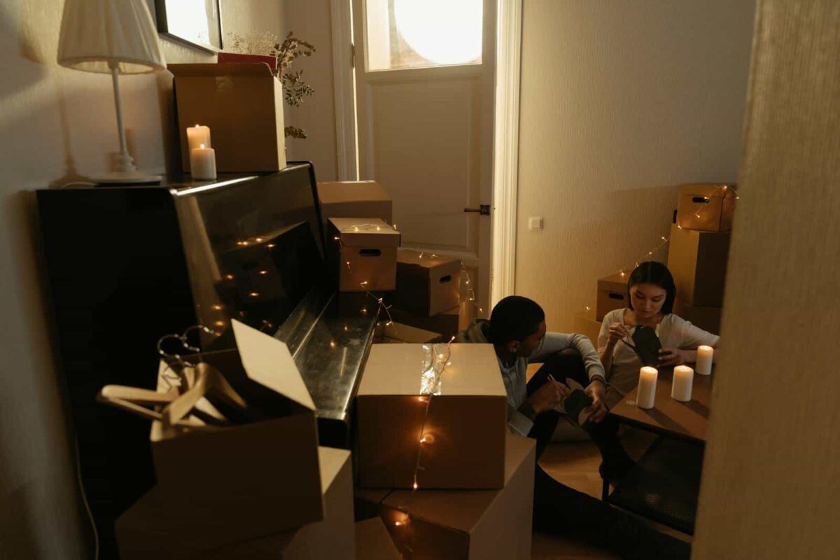 A couple relaxing with candles amidst cardboard boxes, indicating moving or relocation.