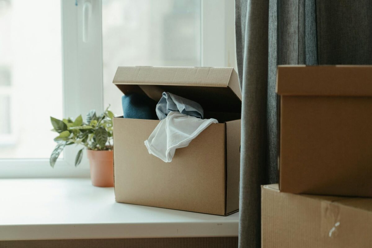 Open cardboard box with clothes by window, symbolizing moving or relocation.