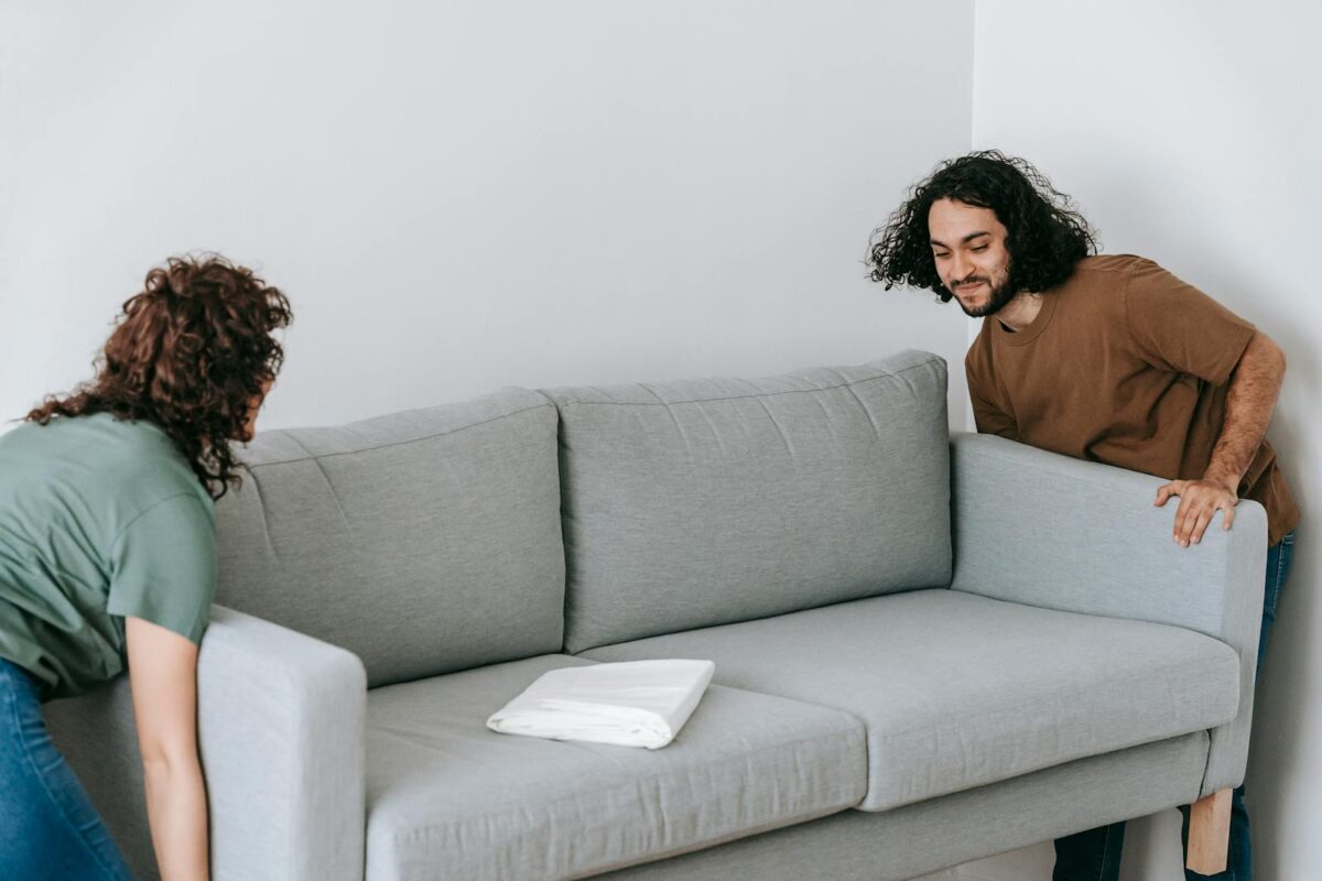 A couple working together to adjust a gray sofa inside a cozy living room space.