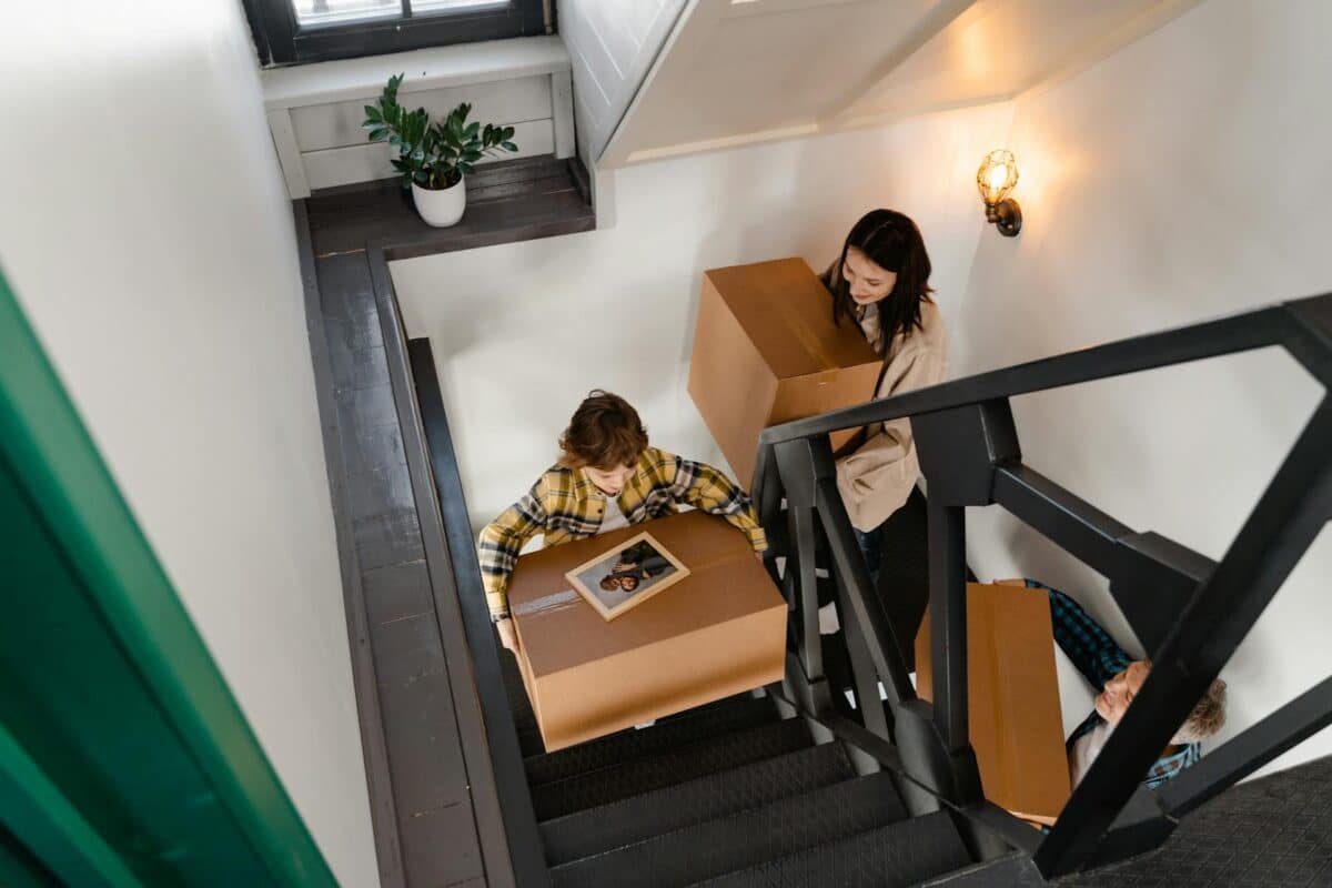 A family carrying moving boxes up stairs, symbolizing a new home beginning.
