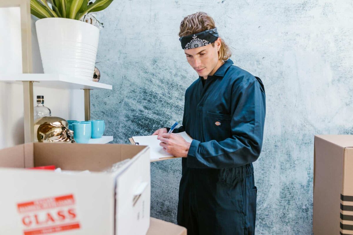 Man wearing overalls and bandana preparing for a home move, surrounded by boxes and fragile items.